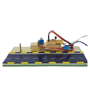 An electronic circuit board kit mounted on a printed wooden road base with yellow and black markings, featuring multicolored wires and small electronic components, isolated on a white background.