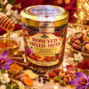 A jar of Go Munch by Go Science Honey Mixed Nuts is beautifully styled on a marble surface with a golden honeycomb lid, surrounded by nuts, cinnamon, turmeric, and a dripping honey dipper.
