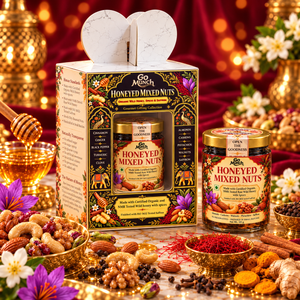 Go Munch by Go Science Honeyed Mixed Nuts gift set displayed with its illustrated outer box, a jar of mixed nuts, and a loose jar beside it on a decorated tabletop. The scene includes bowls of nuts, spices, a honey dipper, flowers, and a red fabric backdrop with warm bokeh lights.