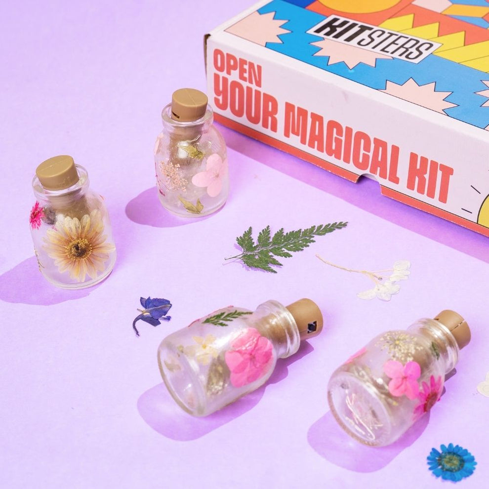 Glass bottles with flowers and leaves next to a colorful 'Kitster' box on a purple background. Kitsters DIY Floral Glow Jar Kit available at Go Science product image 1