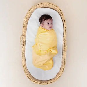 Baby swaddled in yellow cloth lying in a wicker basket with a white mattress. Nintara Organic Cotton Wake Me Not Swaddle 0-3 Months Butter Blossoms Go Littles product main image