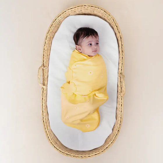 Baby swaddled in yellow cloth lying in a wicker basket with a white mattress. Nintara Organic Cotton Wake Me Not Swaddle 0-3 Months Butter Blossoms Go Littles product main image