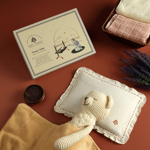 Baby pillow product  including a knitted toy, blanket, and card on a brown surface.