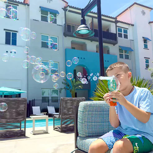 Child blowing bubbles in a residential area with a pool and chairs. Butterfly edufields_4_in_1_Motor_Play_at_Go_Science_Product_image_11