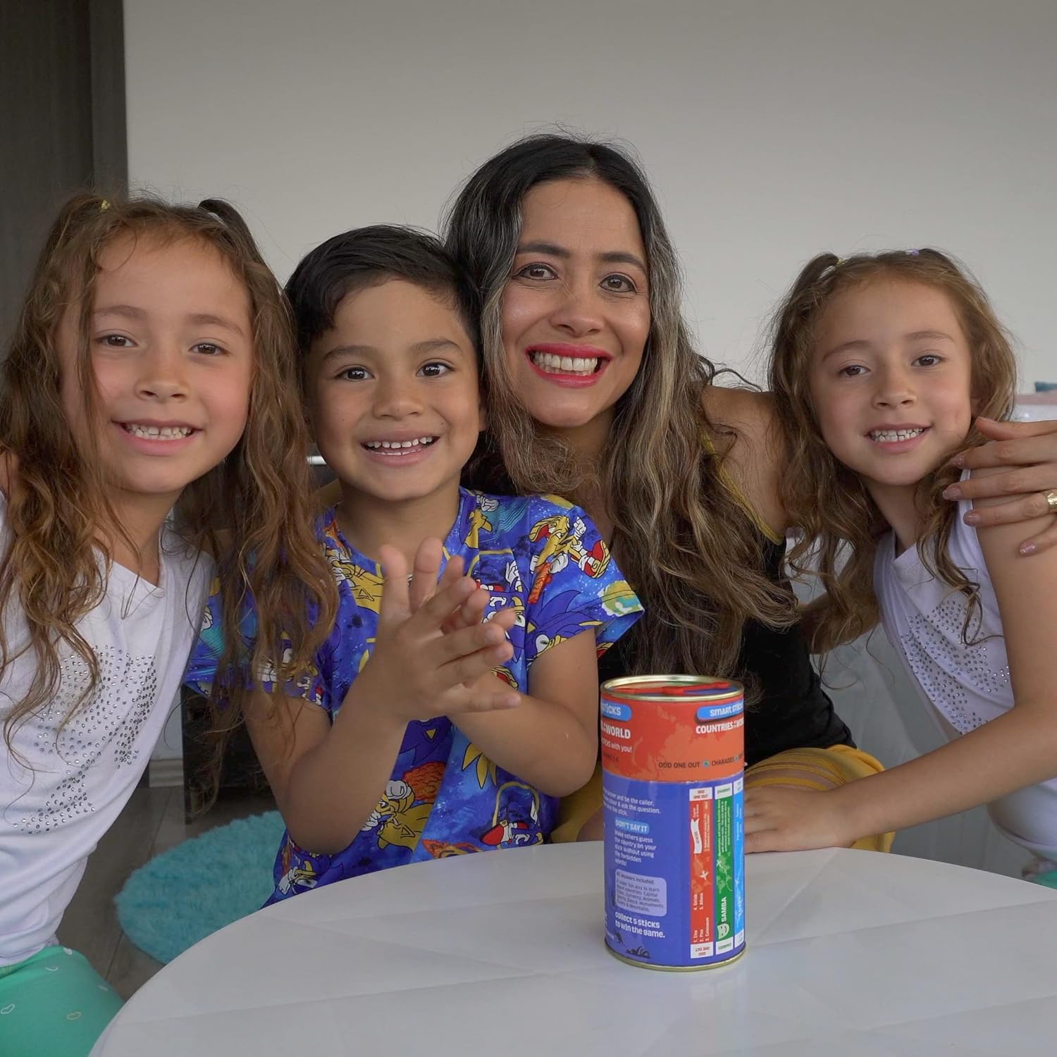 Woman with three children sitting around a table with a colorful canister  of chalk and chuckles game on it.