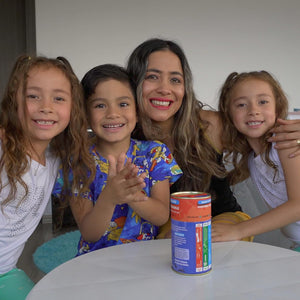 Woman with three children sitting around a table with a colorful canister  of chalk and chuckles game on it.
