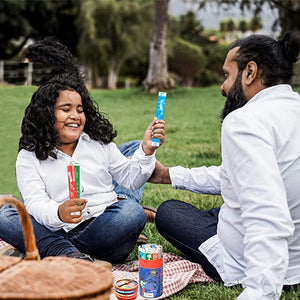 Two people sitting on grass outdoors, holding colorful Chalk & Chuckles Smart Sticks Countries of The World Trivia & Geography Card Game for Kids.