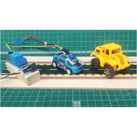 GO Science Classroom Series Obstacle Detection Alarm kit retail box of School project & demonstration kit image 1. A small blue toy car with a mounted camera is shown on a miniature road track alongside a yellow toy truck, with wiring and a blue electronic control unit attached. The setup is photographed on a green cutting mat background.