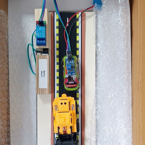 A DIY electronic toy construction vehicle control board inside its foam packaging box. The board features a yellow remote-controlled toy excavator, a black and yellow striped track, a blue relay module labeled 'Power Motor', and a green motor module, connected with multicolored wires. GO Science Classroom Series Obstacle Detection Alarm kit retail box of School project & demonstration kit image 2