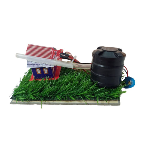 A small electronic model or kit setup on a white background, featuring green artificial grass, a black cylindrical component, a red-and-blue house-shaped module, a clear tube, and a blue circular part on a base. GO Science Classroom Series Rainwater Harvesting Model & Rain Alarm school project kit image 1