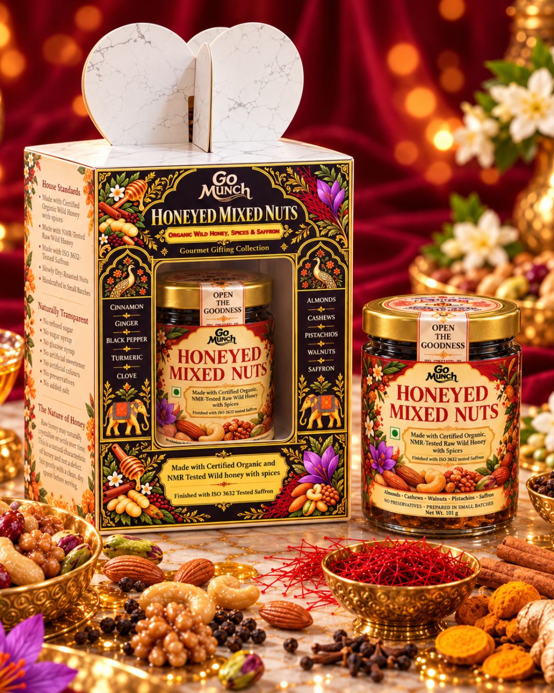 Go Munch by Go Science Honeyed Mixed Nuts gift set displayed with its illustrated outer box, a jar of mixed nuts, and a loose jar beside it on a decorated tabletop. The scene includes bowls of nuts, spices, a honey dipper, flowers, and a red fabric backdrop with warm bokeh lights.