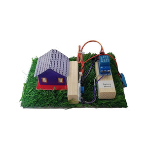 A small electronic model setup on a white background, featuring a miniature house with a purple body and gray roof, artificial green grass, two wooden blocks, wires, and a blue electronic component labeled 'Battery Mount'. From Go Science Classroom Series Fire Alarm Using Flame Sensor School Project & Demonstration Model kit 