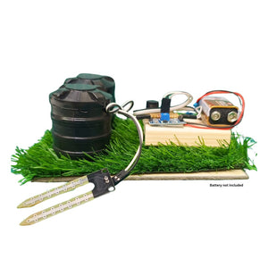 Go Science Classroom Series Smart Soil Moisture Detection kit for School Project & Demonstration kit model image 1. A miniature toy or model vehicle setup displayed on a white background, featuring a black cylindrical body, green artificial grass, a wooden base, a small circuit board, a battery, and two long metal claws. Text on the image reads 'Battery not included'.