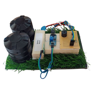 Go Science Classroom Series Smart Soil Moisture Detection kit for School Project & Demonstration kit model image 2. An electronic DIY project kit featuring two black cylindrical battery containers, a wooden battery mount, a breadboard circuit, a blue microcontroller, and green artificial grass on a white background.