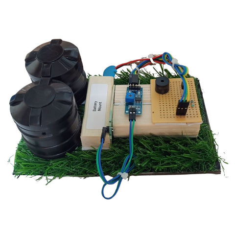 Go Science Classroom Series Smart Soil Moisture Detection kit for School Project & Demonstration kit model image 2. An electronic DIY project kit featuring two black cylindrical battery containers, a wooden battery mount, a breadboard circuit, a blue microcontroller, and green artificial grass on a white background.