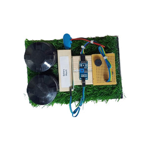 Go Science Classroom Series Smart Soil Moisture Detection kit for School Project & Demonstration kit model image 3. A small electronic DIY project kit on a white background, featuring a green artificial grass base with a battery, two black wheels, a blue motor, a breadboard, and a yellow circuit board.