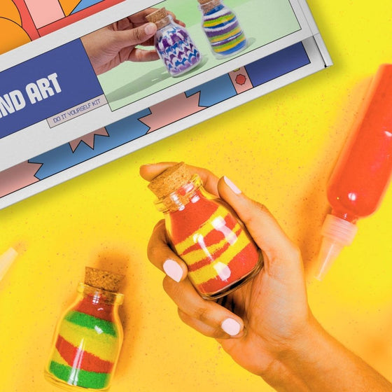 Colorful bottle art kit with small bottles and a design guide on a yellow background. Kitsters DIY Sand Art Kit available at Go Science product image 1