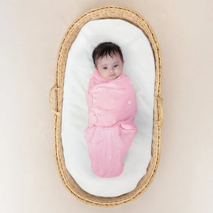 Baby wrapped in a pink swaddle blanket lying in a wicker basket on a beige background. Nintara_Wake_Me_Not_Swaddle_Pretty_Petals_for_0_to_3_Months_go_littles_product_image_1