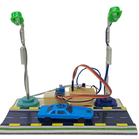 A Smart Street Light school project  DIY electronic car race control kit featuring a blue toy car on a road base, a breadboard circuit board, a microcontroller, and two green LED street light sensors on silver poles.