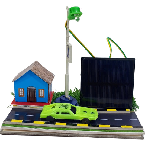 Solar Street light school project go science classroom series. A miniature solar-powered toy city scene on a white background, featuring a blue house, a green car, a street lamp, and a large black solar panel mounted on a base with a road and grass.