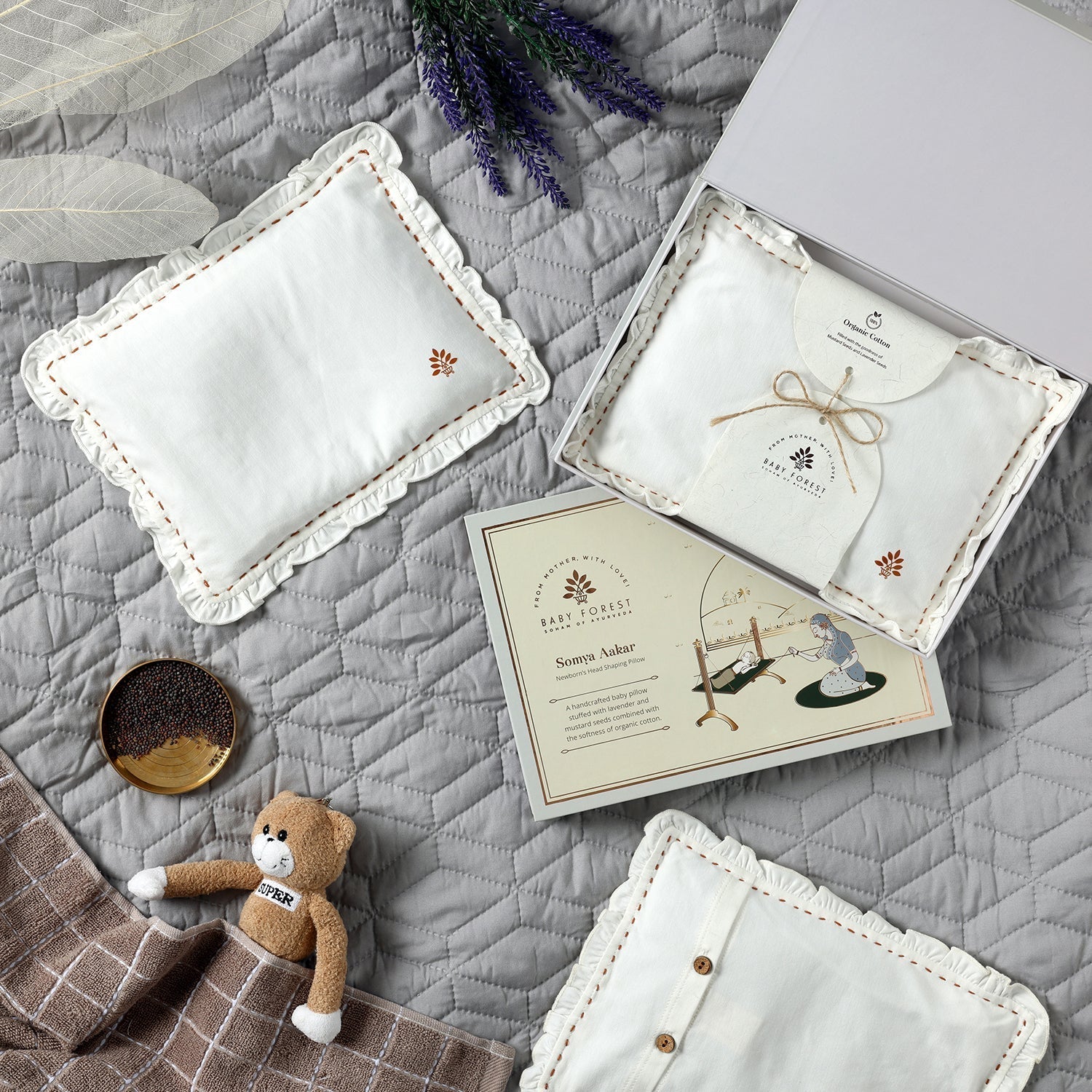 Baby accessories including pillows and a card on a textured surface with lavender flowers.