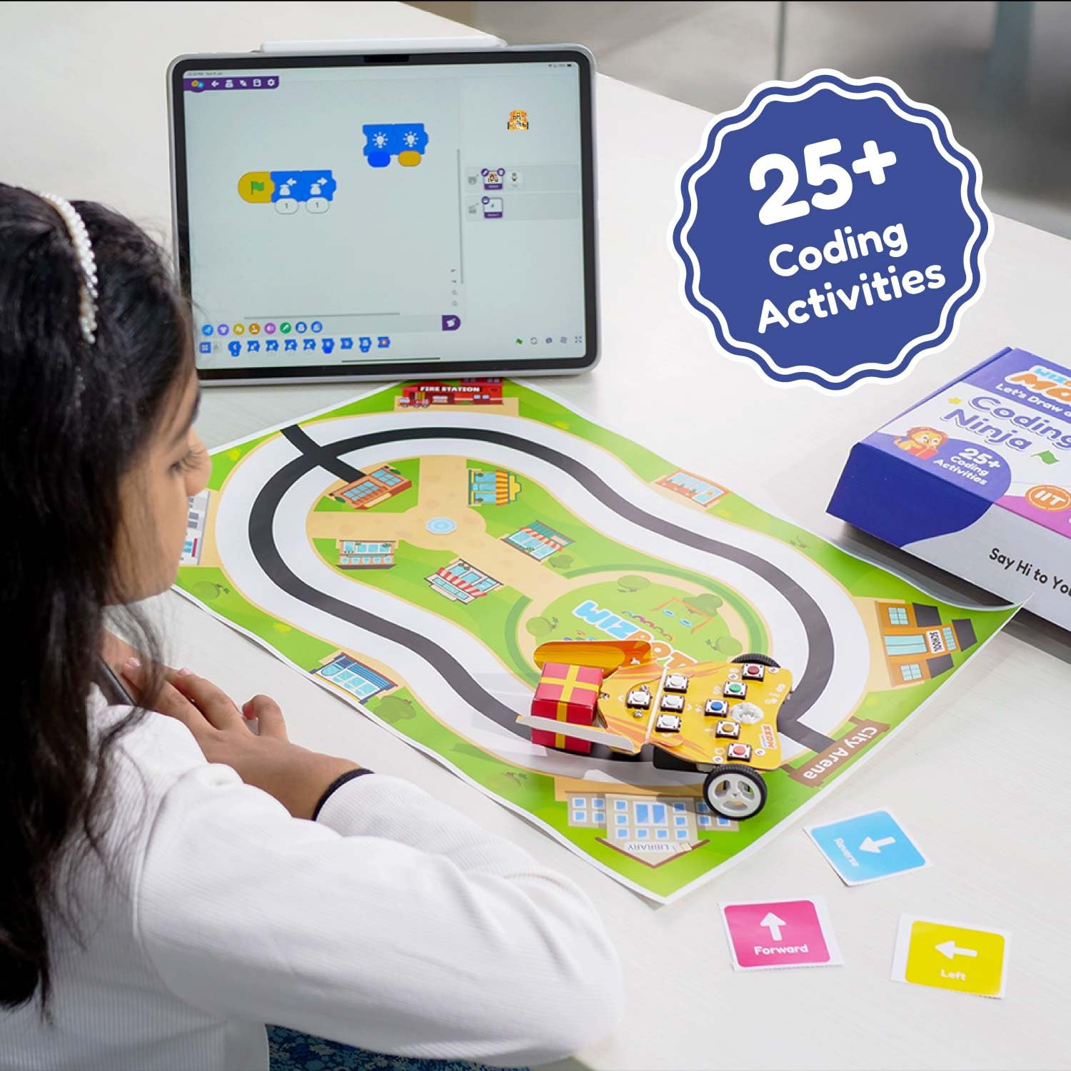 Child playing with a coding mat and toy car on a table, with a tablet displaying coding activities. Stempedia Wizbot Maxx Coding Ninja robot kit Coding kit for Kids  product image 5 available at go science